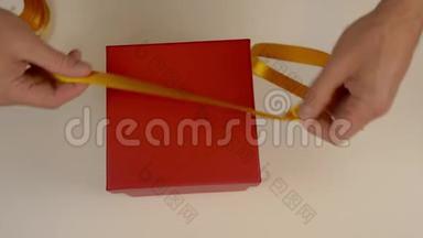 准备礼品包装。 一个红色的纸板箱。 男士双手测量金色缎带装饰礼品盒